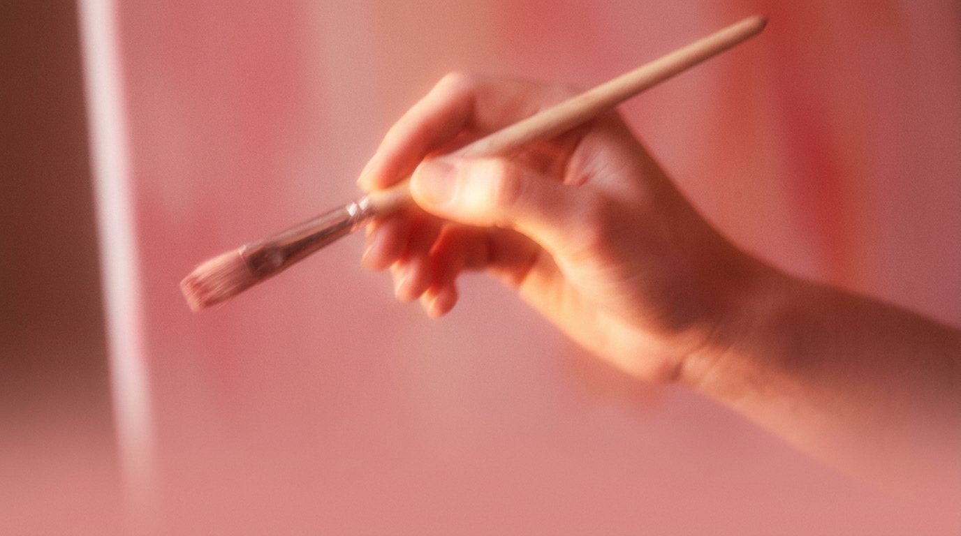 Hand mit Pinsel vor korallenfarbener Fläche
