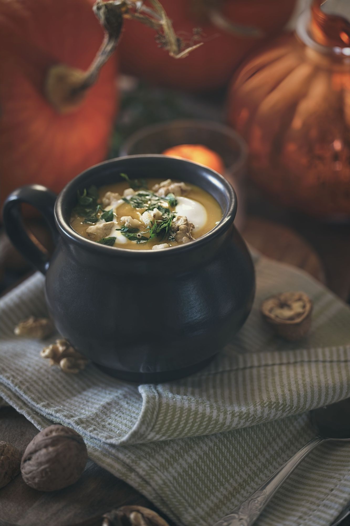 Kürbissuppe in einem schwarzen Keramiktopf vor Kürbissen