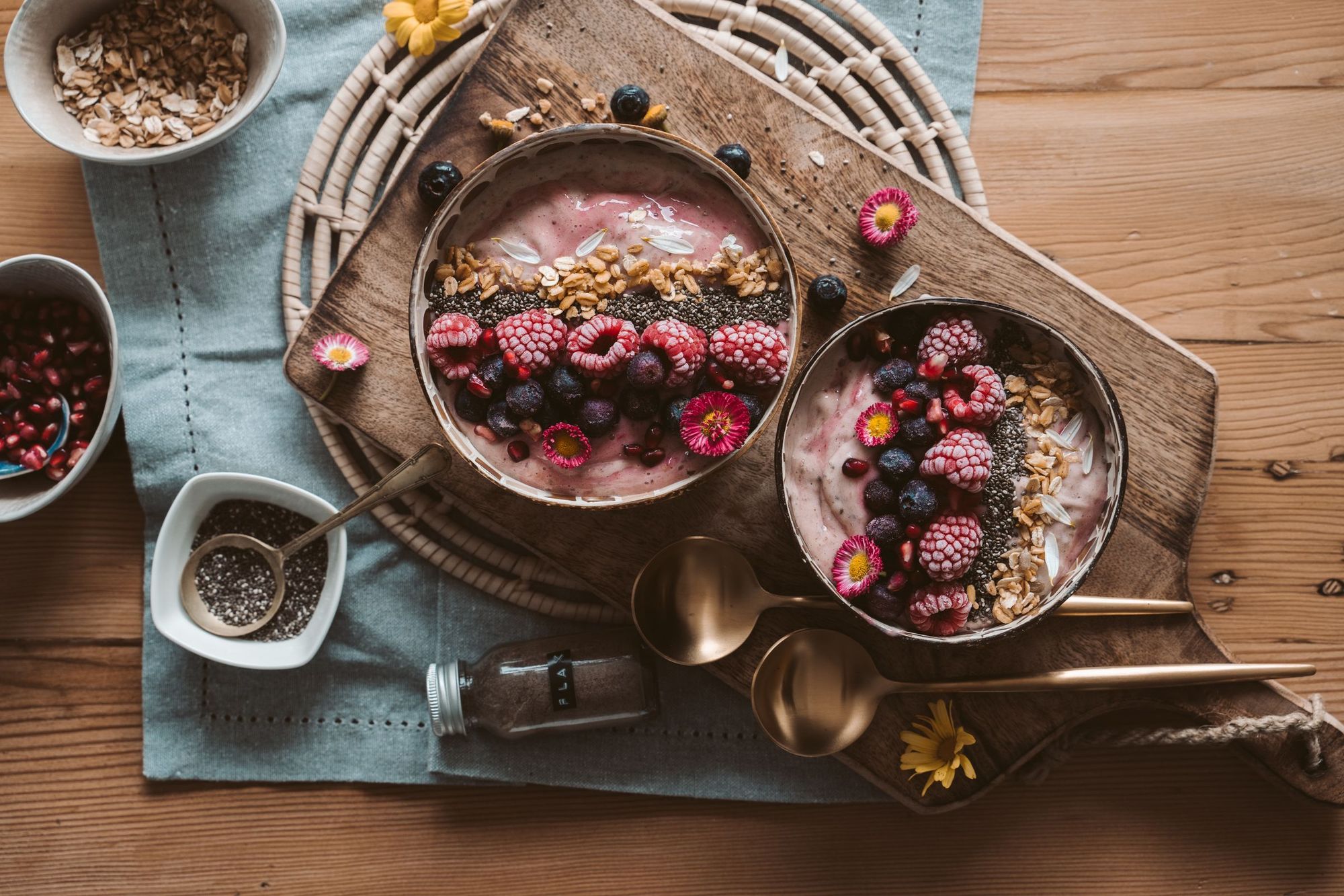 Zwei Smoothie-Bowls mit Beeren und Granola auf einem Holzbrett