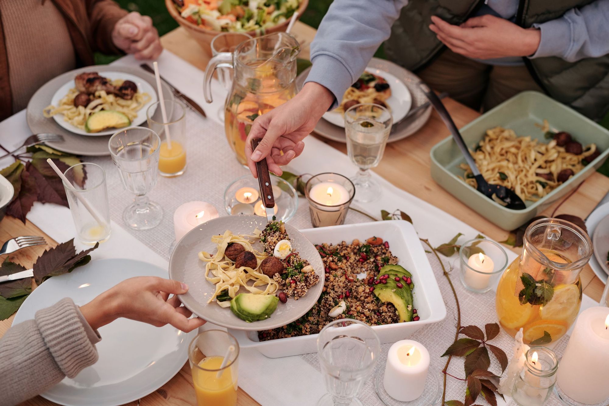 Freunde teilen ein Abendessen bei Kerzenlicht mit Pasta, Salat und Getränken